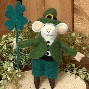 May include: A white felt mouse wearing a green felt hat with a gold buckle and a green felt suit holding a green felt shamrock.