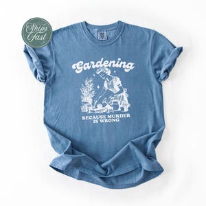 Peut inclure: Un t-shirt bleu avec un motif blanc indiquant "Jardiner parce que le meurtre est mal". Le motif repr&eacute;sente une personne en train de jardiner. Le t-shirt a des manches courtes et un col rond.