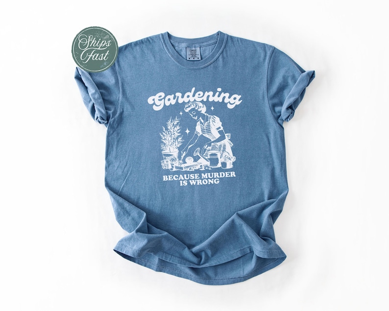 Peut inclure: Un t-shirt bleu avec un motif blanc indiquant "Jardiner parce que le meurtre est mal". Le motif repr&eacute;sente une personne en train de jardiner. Le t-shirt a des manches courtes et un col rond.