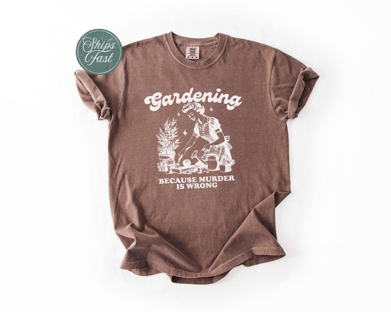 Peut inclure: T-shirt marron avec l'inscription blanche "Gardening Because Murder Is Wrong". Le graphisme repr&eacute;sente un jardinier s'occupant de plantes. Le t-shirt a un col rond et des manches courtes.