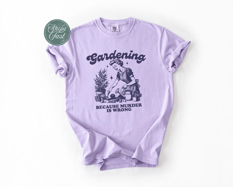 Peut inclure: Un t-shirt lilas clair avec le mot "Gardening" dans une police r&eacute;tro au-dessus d'une illustration d'une femme jardinant. Le texte "BECAUSE MURDER IS WRONG" est en dessous. Le t-shirt a des manches retrouss&eacute;es.