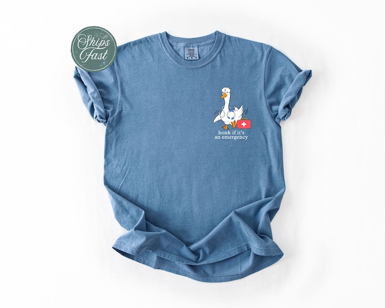 May include: A blue t-shirt featuring a white goose wearing a red first aid kit and the text "honk if it's an emergency".