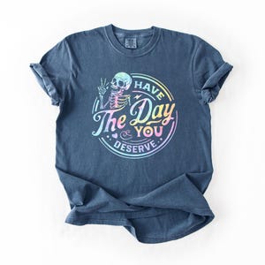 May include: A dark blue t-shirt with a rainbow-colored graphic of a skeleton with the text "Have the Day You Deserve".