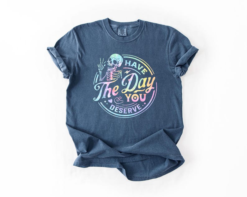 May include: A dark blue t-shirt with a rainbow-colored graphic of a skeleton with the text "Have the Day You Deserve".