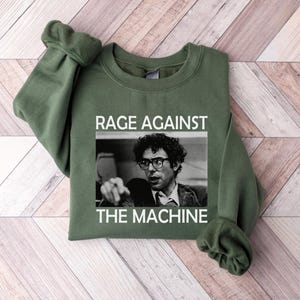 May include: A green sweatshirt with the text "Rage Against The Machine" and a black and white image of a man with glasses.