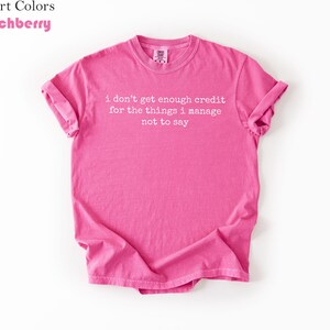 Puede incluir: Una camiseta rosa brillante con las mangas enrolladas. La camiseta presenta el texto "i don't get enough credit for the things i manage not to say" en blanco. La camiseta es de la marca Comfort Colors en color Crunchberry.