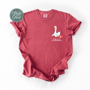 May include: A red t-shirt featuring a white goose graphic and the text "honk if it's an emergency".