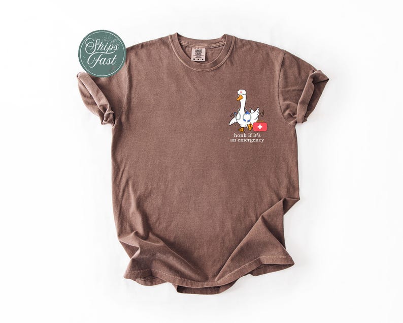 May include: A brown t-shirt featuring a white goose graphic and the text "Honk if it's an emergency".