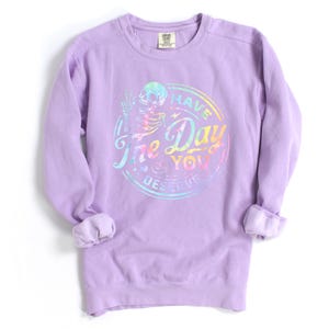 May include: A lavender long-sleeved sweatshirt with a rainbow tie-dye design featuring a skull and the text "Have the Day You Deserve".