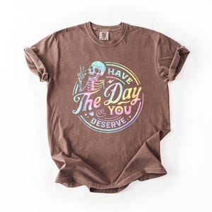 May include: Brown t-shirt with a rainbow iridescent graphic of a skeleton with the text "Have the Day You Deserve."