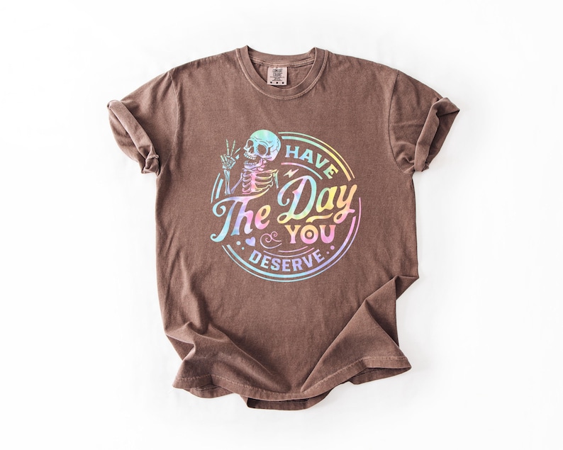 May include: Brown t-shirt with a rainbow iridescent graphic of a skeleton with the text "Have the Day You Deserve."