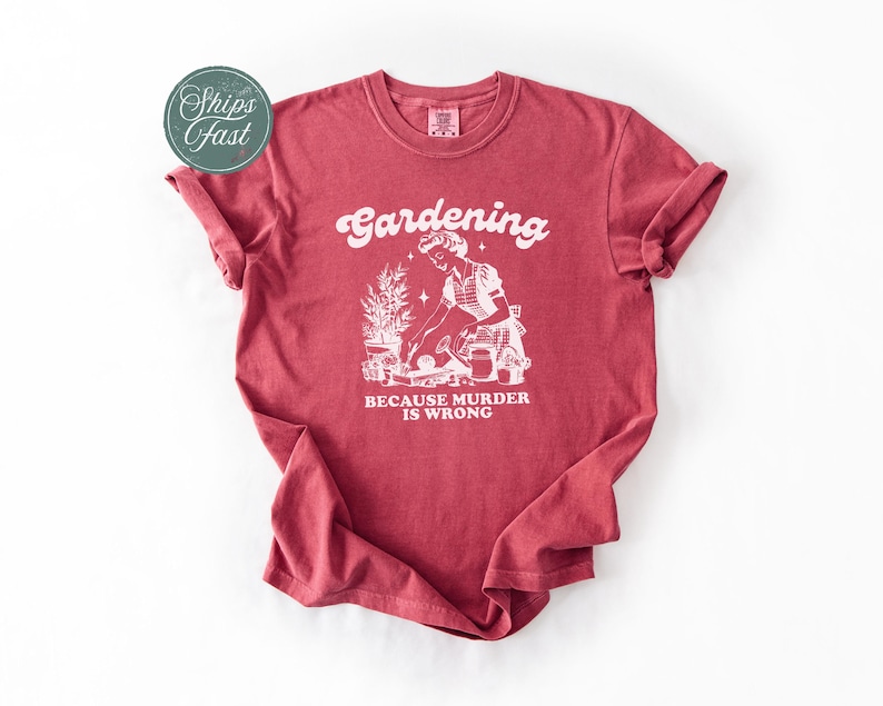 Peut inclure: T-shirt rouge avec l'inscription blanche "Gardening" et "BECAUSE MURDER IS WRONG". Le t-shirt pr&eacute;sente une illustration blanche d'une personne jardinant.