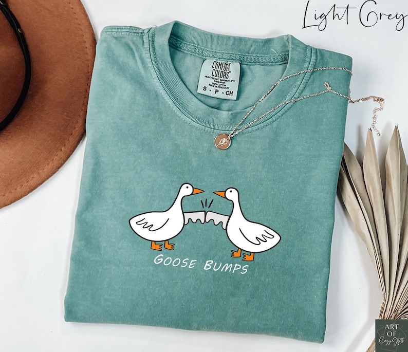 May include: A light green t-shirt with a white goose design and the text "GOOSE BUMPS". The shirt is made of a soft, comfortable material.