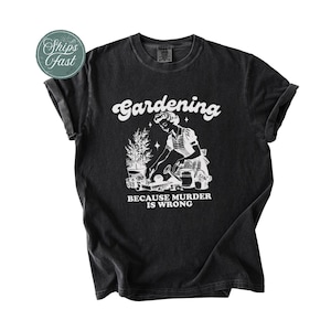 Peut inclure: T-shirt noir avec un motif blanc repr&eacute;sentant une femme jardinant, accompagn&eacute; du texte "Gardening because murder is wrong". Le t-shirt a des manches retrouss&eacute;es et un col rond.
