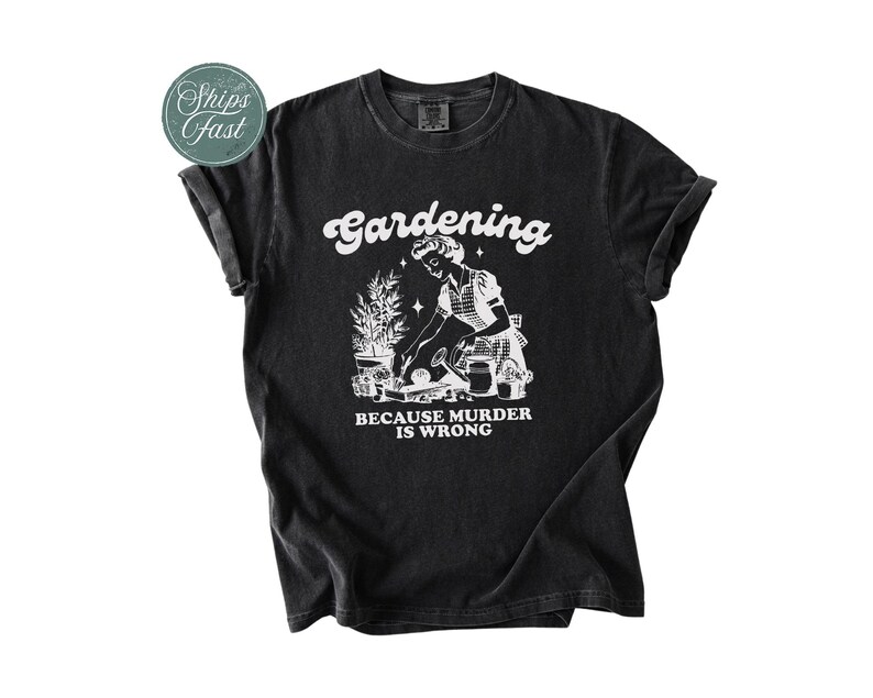 Peut inclure: T-shirt noir avec un motif blanc repr&eacute;sentant une femme jardinant, accompagn&eacute; du texte "Gardening because murder is wrong". Le t-shirt a des manches retrouss&eacute;es et un col rond.