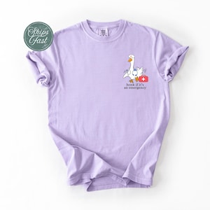 May include: A lavender t-shirt featuring a cartoon goose holding a first aid kit. The text on the shirt reads "Honk if it's an emergency".