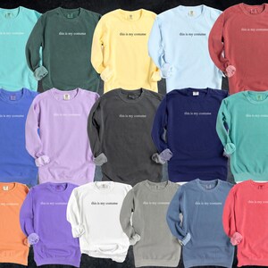 May include: A collection of long-sleeved sweatshirts in various colors, including teal, green, yellow, light blue, and red. Each sweatshirt has the phrase "this is my costume" printed in white across the chest. The sleeves are cuffed.