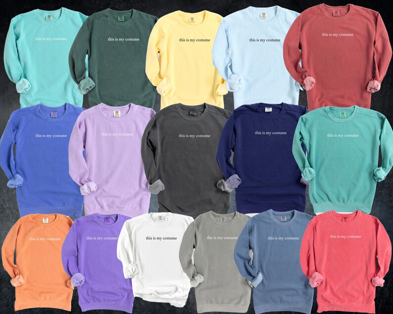 May include: A collection of long-sleeved sweatshirts in various colors, including teal, green, yellow, light blue, and red. Each sweatshirt has the phrase "this is my costume" printed in white across the chest. The sleeves are cuffed.