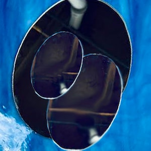 May include: Two round, black, reflective mirrors, one slightly larger than the other, are nested inside each other. The mirrors are set against a blue background.