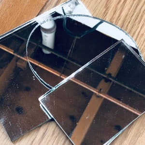 May include: Three pieces of broken mirror glass, one round and two rectangular, reflecting the surrounding environment.