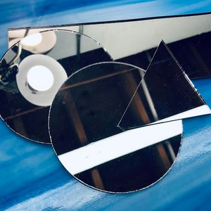 May include: Three black reflective surfaces, a rectangle, a circle, and a triangle, are arranged on a blue background. The surfaces are reflecting light and creating interesting patterns.