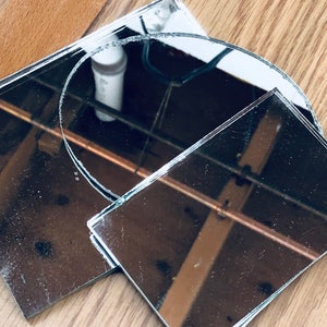 May include: Three pieces of broken mirror glass, one round and two rectangular, on a wooden surface.