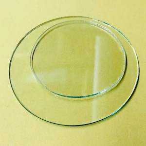 May include: Two clear glass circles, one nested inside the other, on a yellow background. The outer circle is larger, with a diameter of approximately 6 inches. The inner circle is smaller, with a diameter of approximately 4 inches. The glass is transparent.