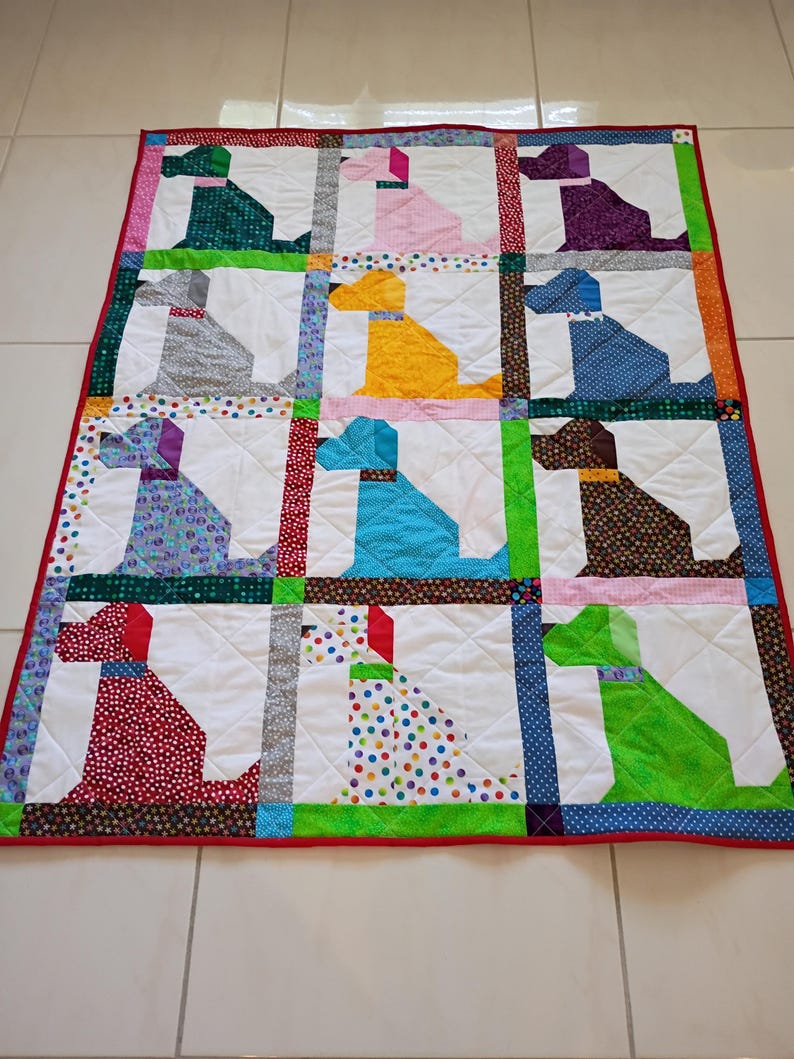 May include: A rectangular patchwork quilt featuring a grid of twelve dog silhouettes in various colors and patterns, including green, pink, purple, gray, yellow, blue, brown, red, and polka-dot fabrics, all set against white backgrounds with a red border.