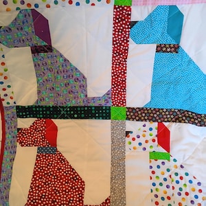 May include: A patchwork quilt featuring four stylized dog silhouettes crafted from various colorful fabrics. The dogs are rendered in purple, blue, red, and white with polka dot, floral, and geometric patterns, separated by white quilted sections.
