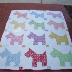 May include: A white quilt with a red border features a repeating pattern of 12 colorful dogs. Each dog is made of a different patterned fabric in shades of pink, yellow, green, blue, and red.