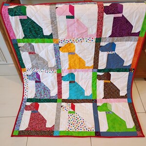 May include: A patchwork quilt featuring a grid of twelve stylized dog silhouettes in various colors and patterns, including green, pink, purple, gray, yellow, blue, brown, red, and polka dots, separated by white fabric and a red border.