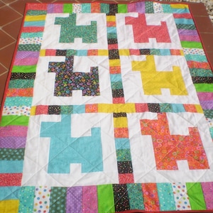 May include: A colorful patchwork quilt with a white background and a repeating pattern of stylized dogs in various colors. The quilt is bordered with strips of fabric in different colors and patterns.