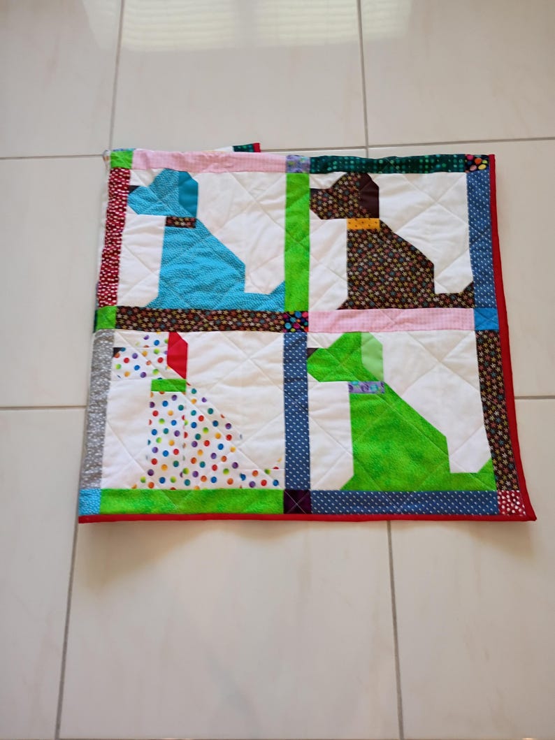 May include: A square patchwork quilt featuring four distinct dog silhouettes in blue, brown, white with colorful polka dots, and green. The quilt is constructed with white fabric blocks, separated by patterned fabric sashing, and finished with a red border.
