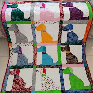 May include: A patchwork quilt featuring a grid of twelve dog silhouettes in various colors and patterns, including green, pink, purple, gray, yellow, blue, brown, and red. The dogs are set against white backgrounds with colorful fabric borders.