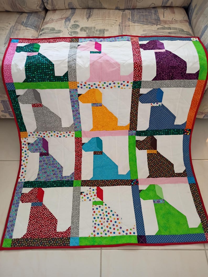 May include: A patchwork quilt featuring a grid of twelve dog silhouettes in various colors and patterns, including green, pink, purple, gray, yellow, blue, brown, and red. The dogs are set against white backgrounds with colorful fabric borders.