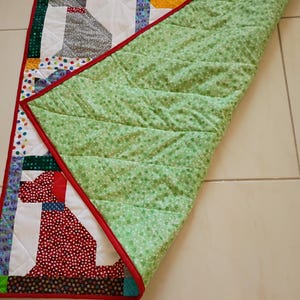 May include: A rectangular patchwork quilt featuring stylized dog silhouettes in various patterned fabrics including red, grey, and yellow. The quilt has a bright red border and a light green backing fabric with a small white floral print pattern.