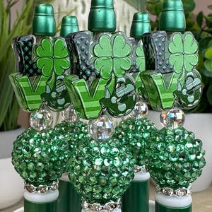 May include: Green bottle stoppers with the word "LOVE" and shamrock designs. The stoppers have a green, jewel-covered ball and a silver band. The tops are green and cylindrical.