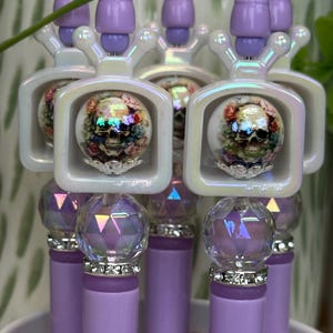 May include: A collection of decorative bottle stoppers. Each stopper features a lavender base, a crystal-like sphere, and a skull design encased in a white, iridescent frame. The skull is adorned with floral accents, creating a unique and artistic aesthetic.