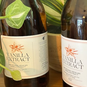 Könnte beinhalten: Zwei braune Glasflaschen Vanilleextrakt mit weißen Etiketten und orangefarbenen floralen Designs. Die Etiketten lauten "Vanilleextrakt" und "100% Bio-Vanilleextrakt aus Mexiko". Die Flaschen sind 237 ml groß und stammen von The Honeypot Homestead.