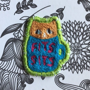 May include: A thank you card with a black and white floral pattern. A small embroidered patch of a cat sitting in a mug with the text "Fits Sits" is attached to the card. The card also includes the text "paperandsewing@etsy".
