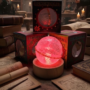 May include: A glowing red Remembrall sphere sits on a wooden base, with a matching box behind it. The sphere has a detailed, swirling design and is lit from within. The box is red and black with the word "Remembrall" printed on it. The scene is set in a library.