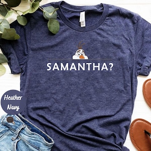 K&ouml;nnte beinhalten: Ein marineblaues T-Shirt mit einer wei&szlig;en Grafik von Olaf aus Frozen, der &uuml;ber eine Linie schaut, unter der der Text "SAMANTHA?" gedruckt ist.