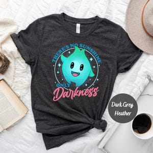 May include: Dark grey heather t-shirt featuring a blue and green cartoon ghost with the text "There's no sunshine only darkness" in a circle around it.
