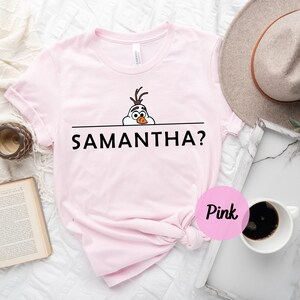 K&ouml;nnte beinhalten: Rosa T-Shirt mit einem Olaf-Cartoon aus Frozen, der &uuml;ber den oberen Rand schaut, und dem Text "SAMANTHA?" auf der Vorderseite.