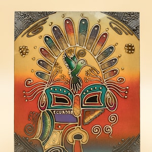 May include: A colorful ceramic tile with a stylized mask design. The mask has a turquoise, green, and red color scheme with a hummingbird in the center. The tile is framed with a silver border and has the word "Ecuador" written on it.
