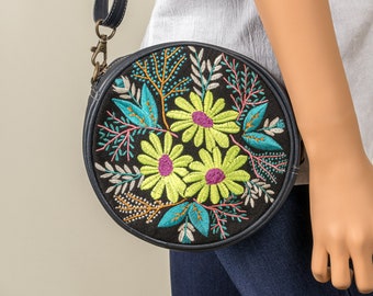 May include: A round black crossbody bag with a floral embroidery design. The embroidery features yellow, green, and pink flowers on a black background.