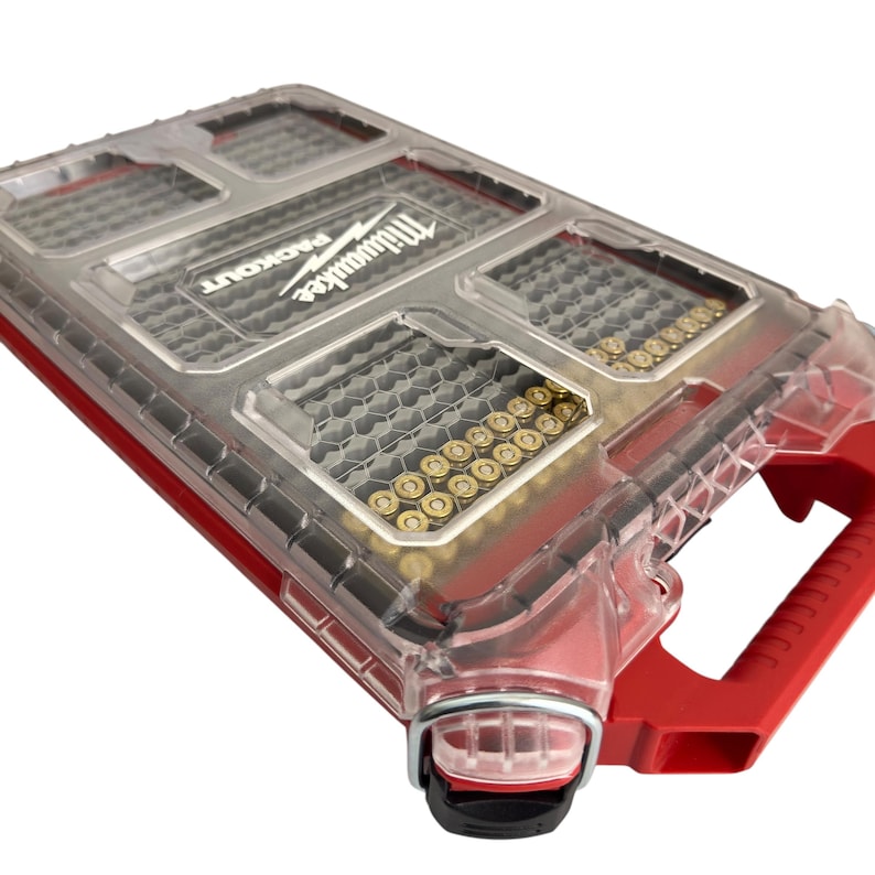 May include: A clear plastic storage case with red accents and a handle. The case is labeled "Milwaukee Packout" and contains multiple rows of gold-colored screws.