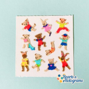 May include: A sheet of vintage stickers featuring various teddy bears and a bunny in colorful outfits. The bears are in different poses, with outfits in red, blue, yellow, and pink. The text "Hearts n Holograms" is in the bottom right corner.