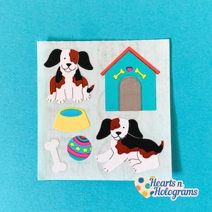 May include: A sheet of dog-themed stickers featuring two brown, black, and white dogs, a turquoise dog house with a red roof, a yellow bowl, a bone, and a colorful ball. The stickers are on a white background with the text "Hearts n Holograms".