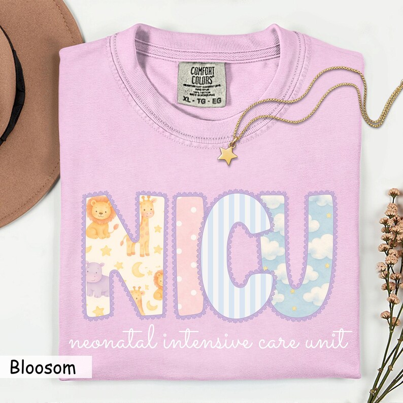 May include: A light purple t-shirt with the letters "NICU" in a decorative font, each letter featuring a different pattern and animal illustrations. The text "neonatal intensive care unit" is below the letters. A gold star necklace rests on the shirt.
